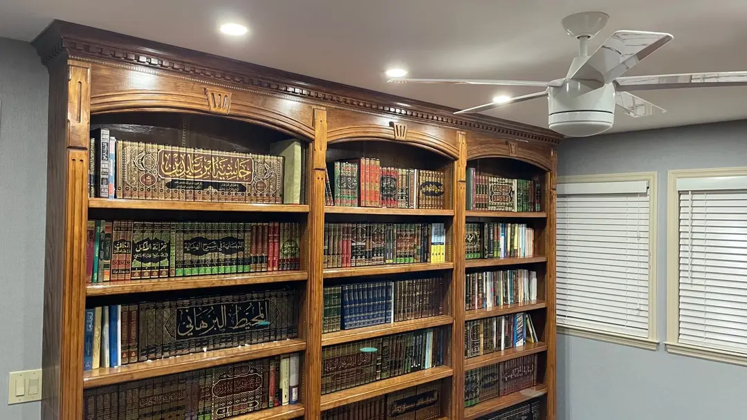 A closer view of the library’s arched bookcases, carved along the top, with multi-volume Arabic works lettered in gold along their spines.